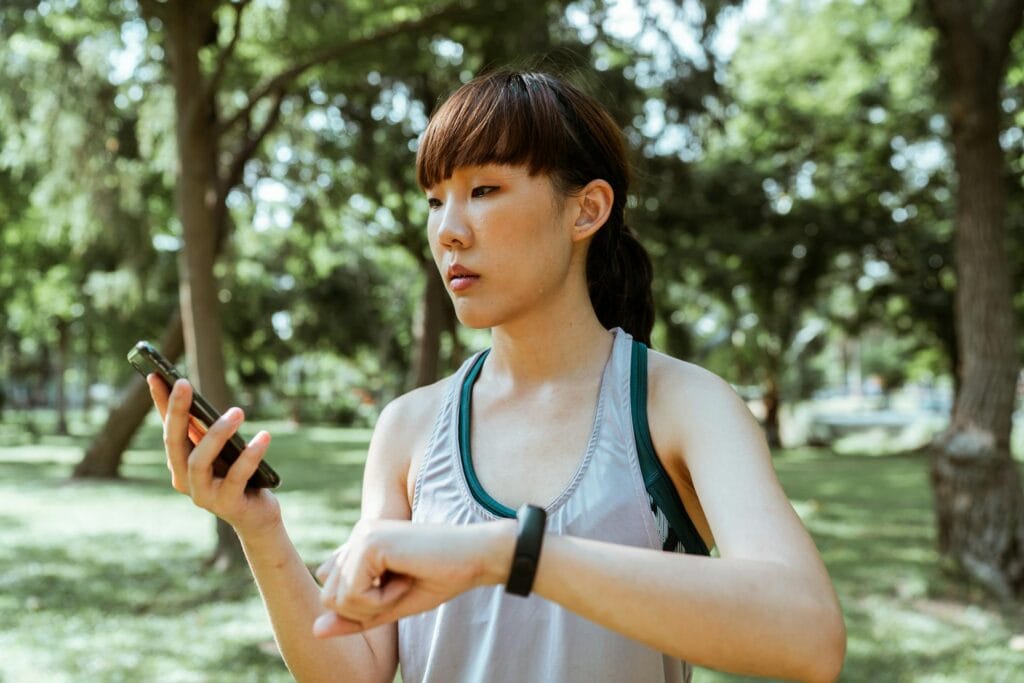 A woman in training clothes checking her phone and watch after a run.