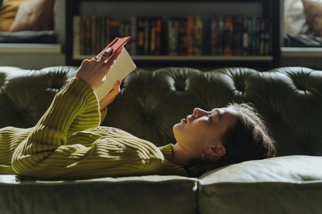 A woman lying on a coach, reading a book.
