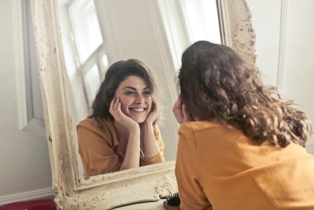 The importance of knowing yourself: A woman smiling to her reflection.
