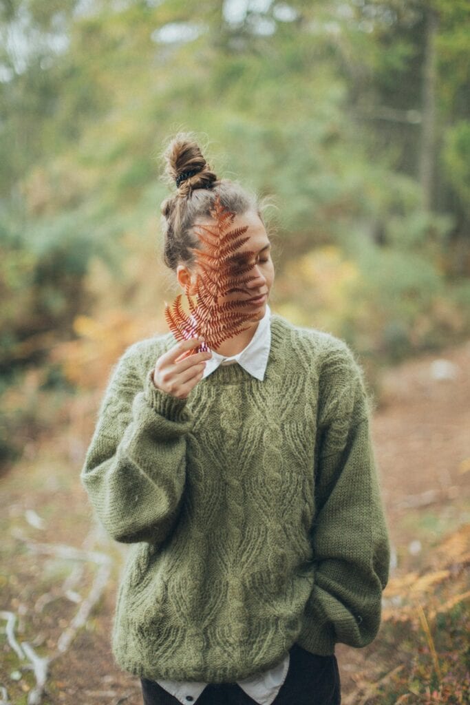 The Importance Of Knowing Yourself: A Woman In The Forest, Holding A Leaf Up To Her Face.