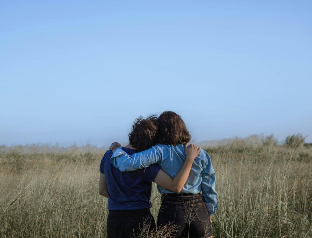 Two women hugging each other in a field of grass.