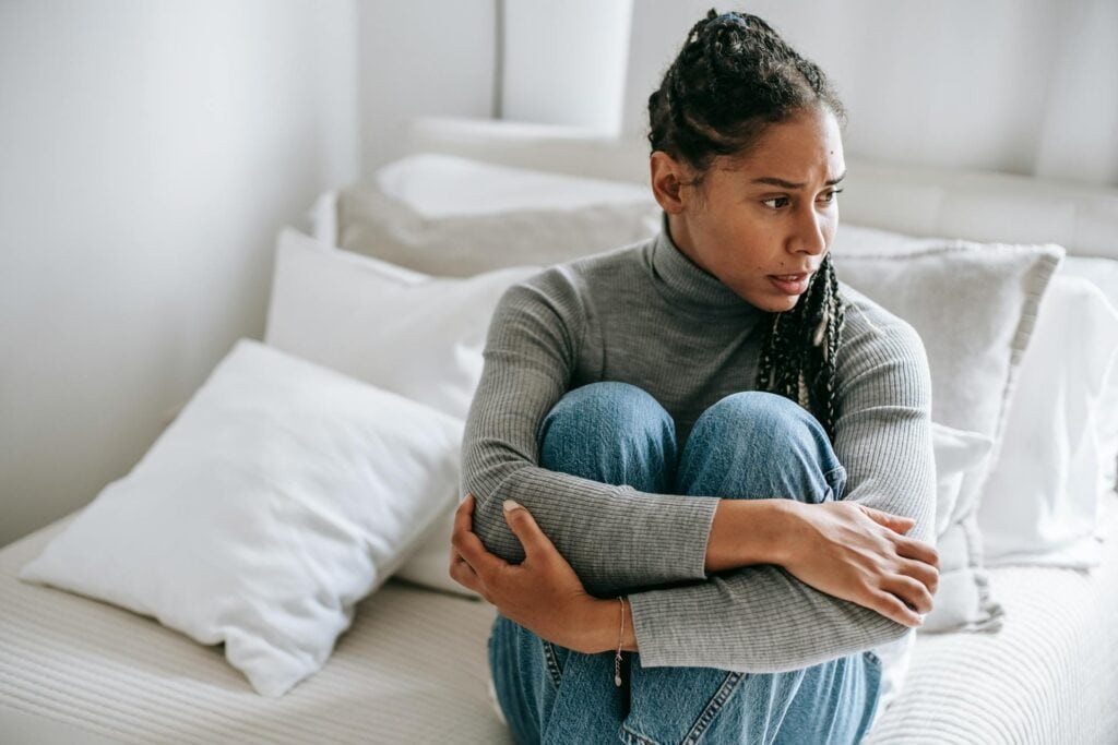 A worried woman sitting on her bed, thinking.