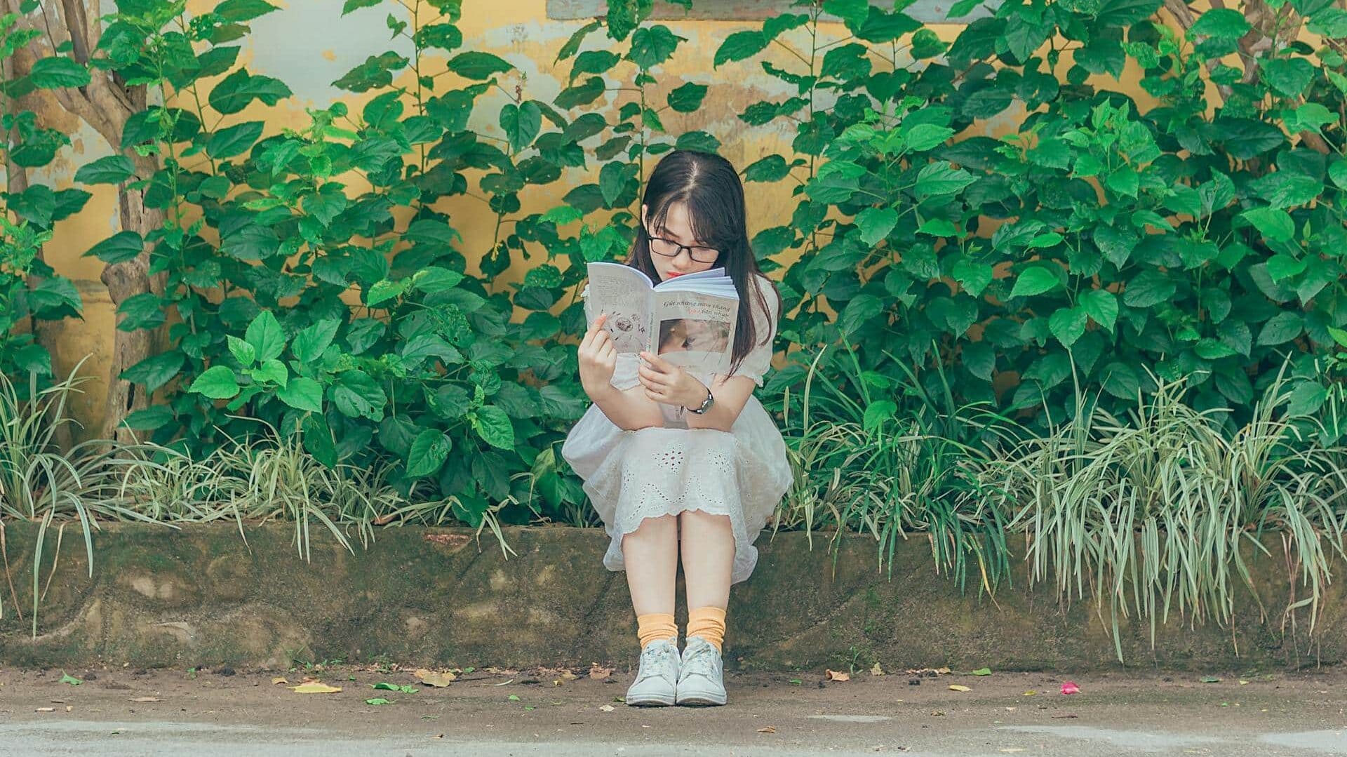 A woman sat in front of a house, reading a book. 