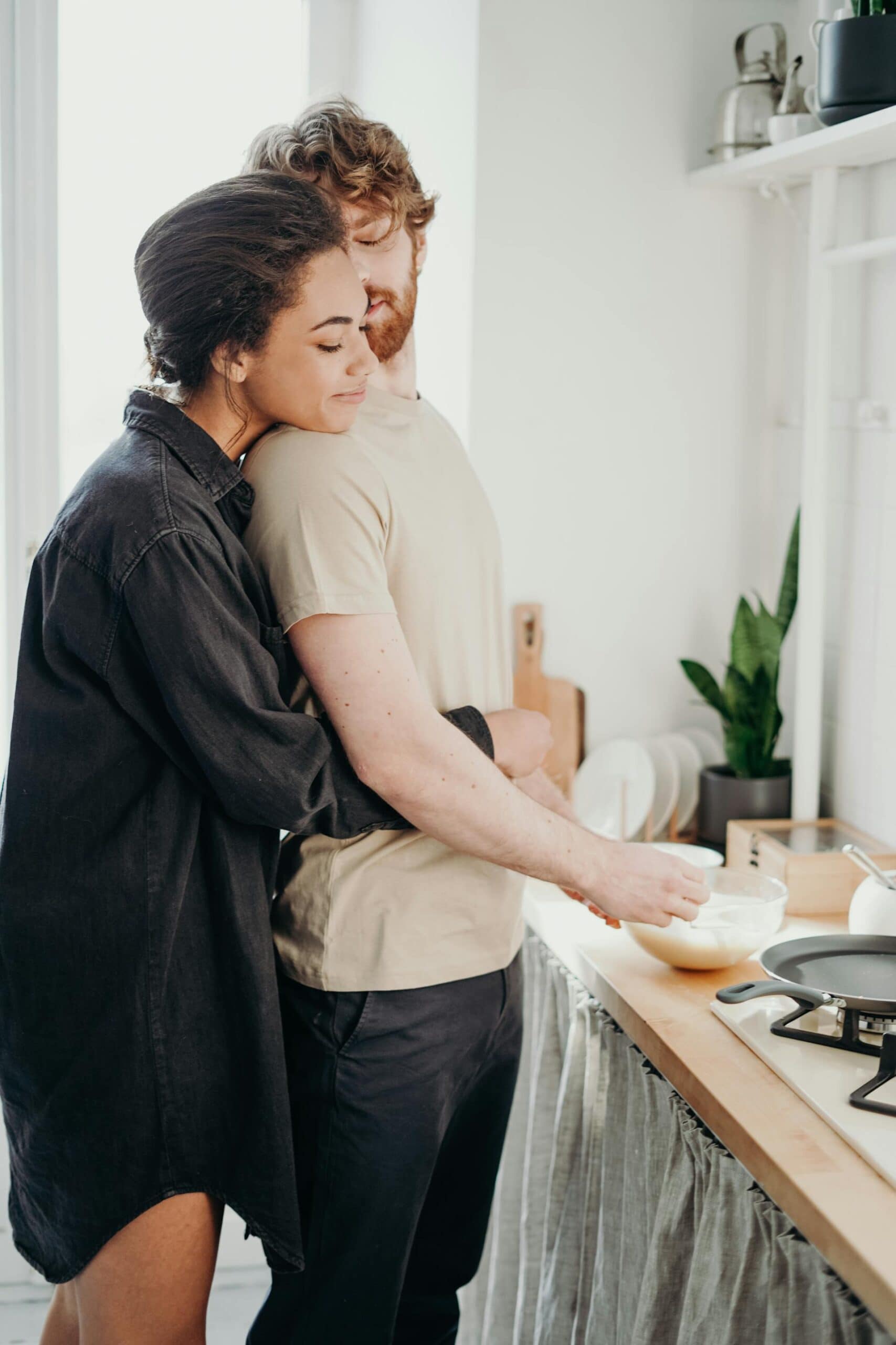Relationship check-in questions: a woman hugging a man in their kitchen.