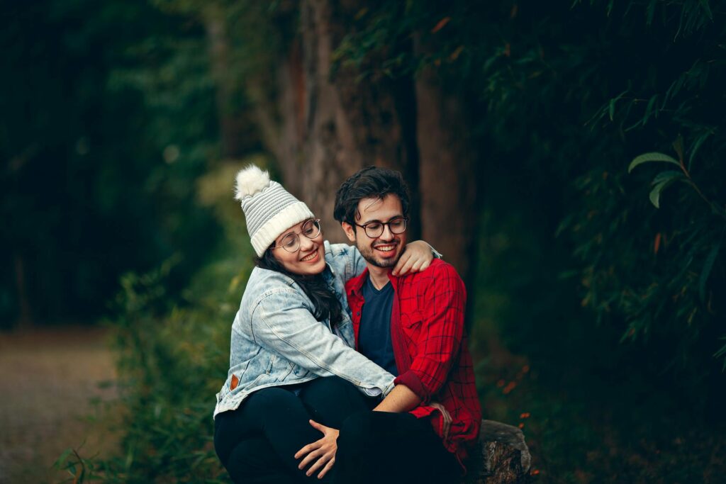 A couple smiling and hugging in the forest.