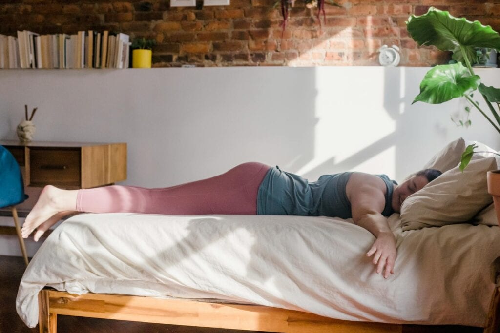 A woman in yoga clothes lying flat on her bed.