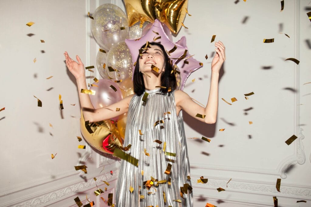 Smiling woman in silver dress with confetti around her - How To Celebrate Yourself: 8 Simple And Joyful Ideas