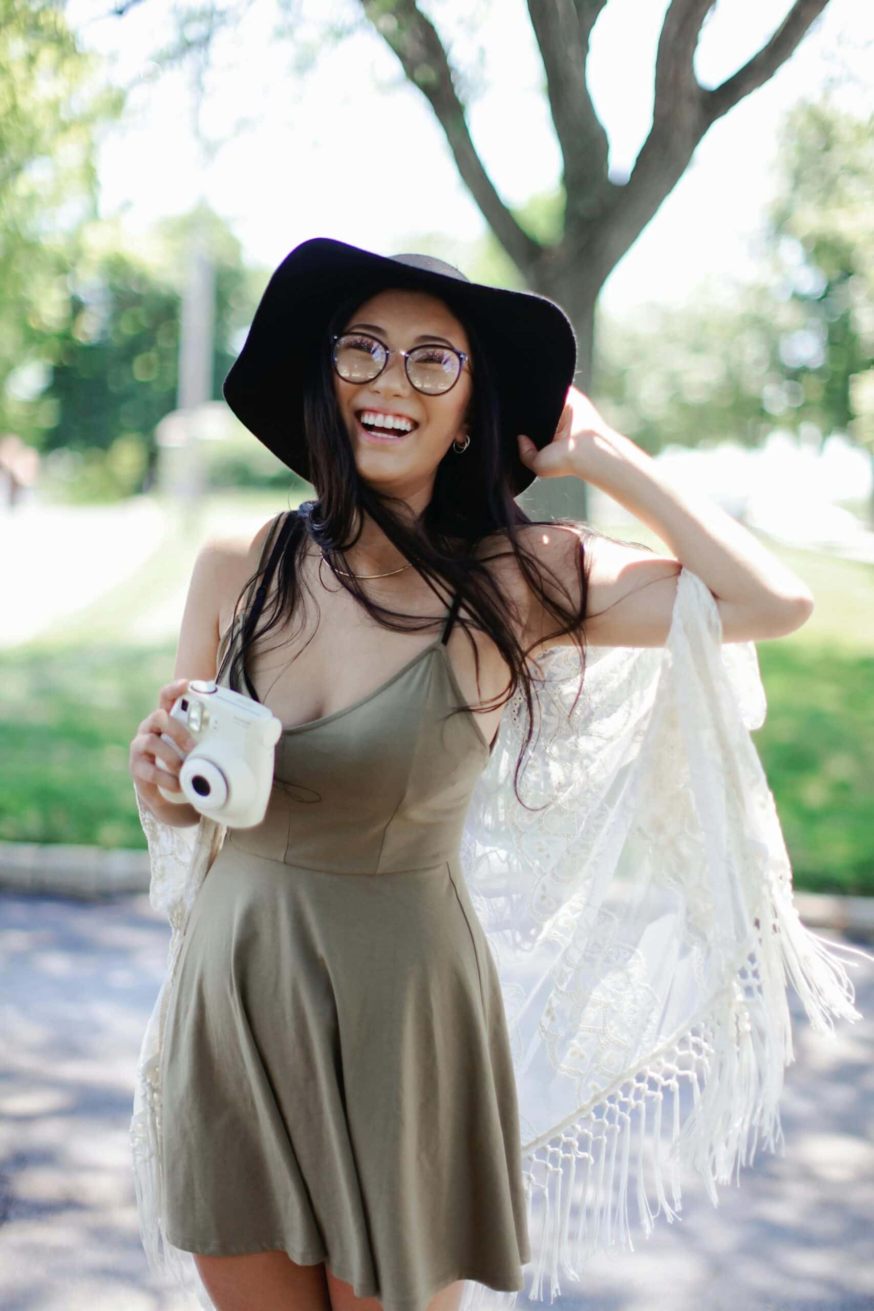 A fashionable woman holds a camera and smiles at the lens.