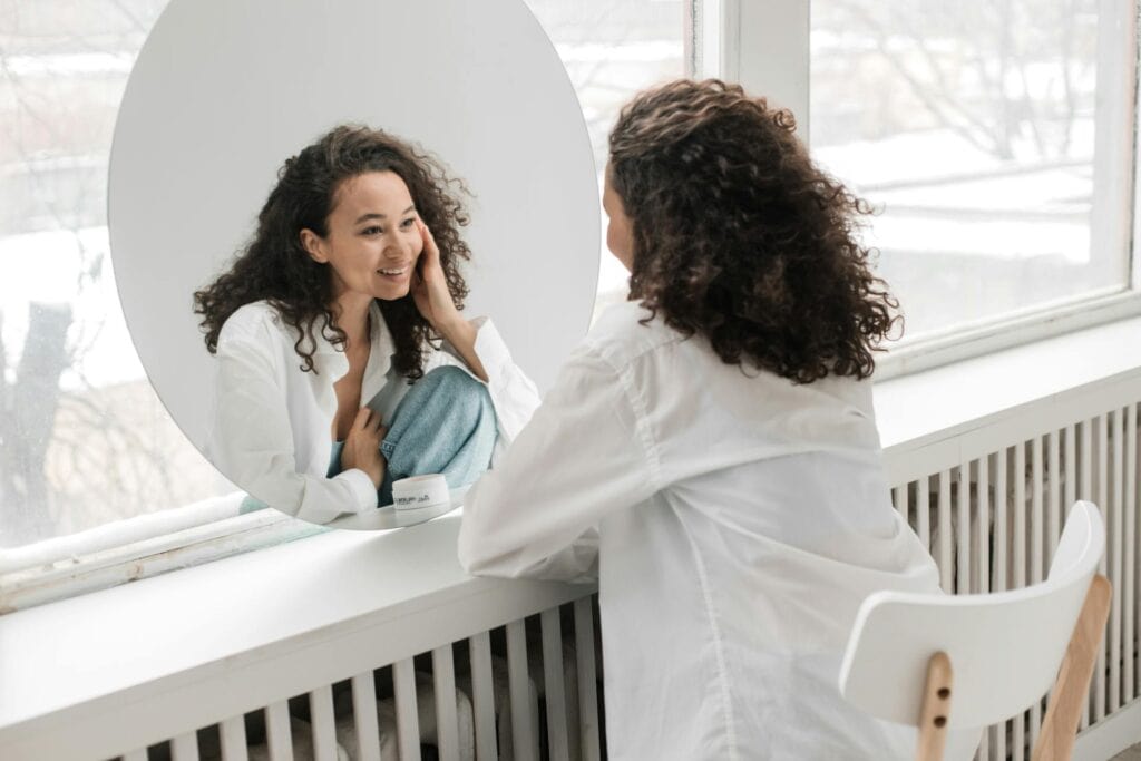 How To Improve Your Self-Esteem As A Woman: 9 Life-Changing Tips - A woman sits on a chair, observing her reflection in the mirror.