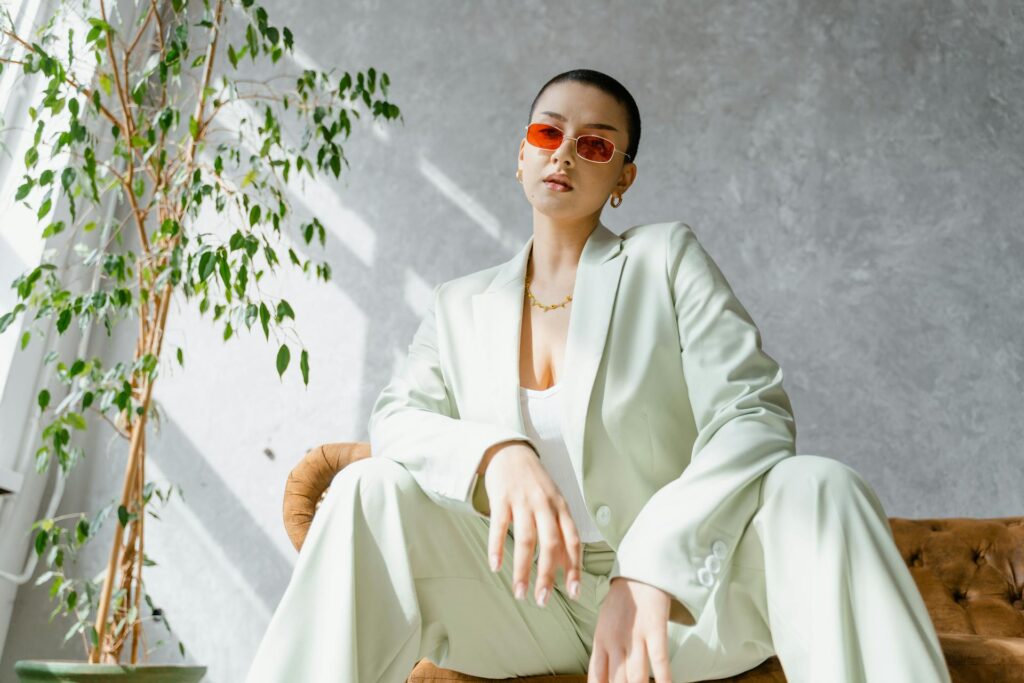 A woman in a green suit and sunglasses poses confidently on a couch for How To Improve Your Self-Esteem As A Woman: 9 Life-Changing Tips