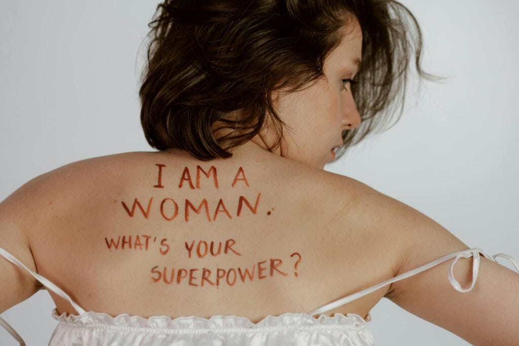 The statement "I am a woman. What's your superpower?" written on a woman's back.