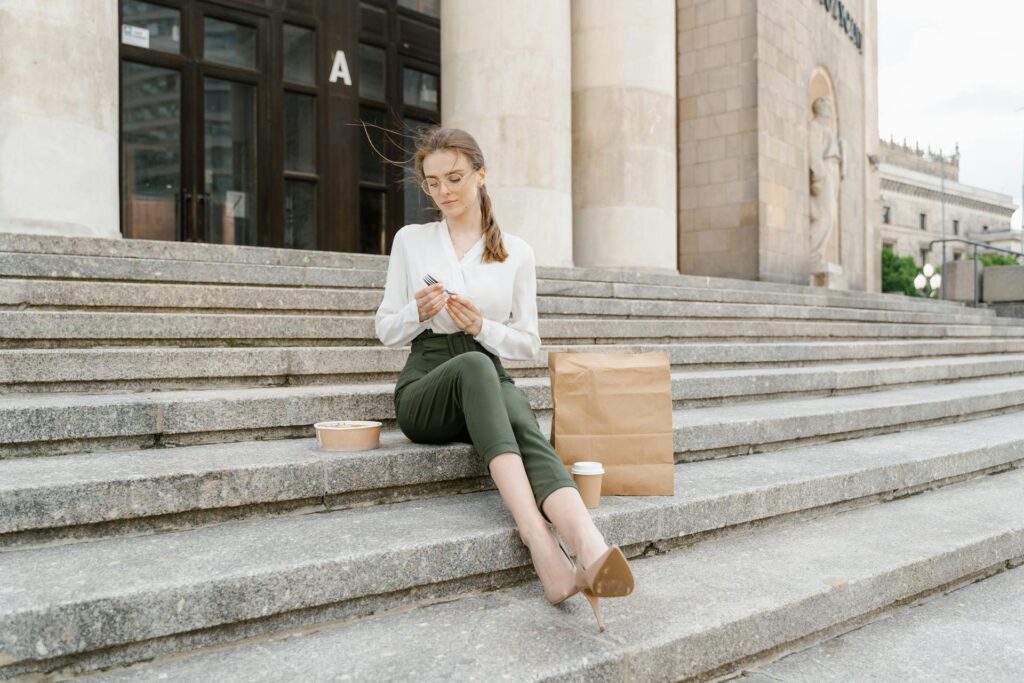 A businesswoman is seated on steps, ready to eat her packed meal.