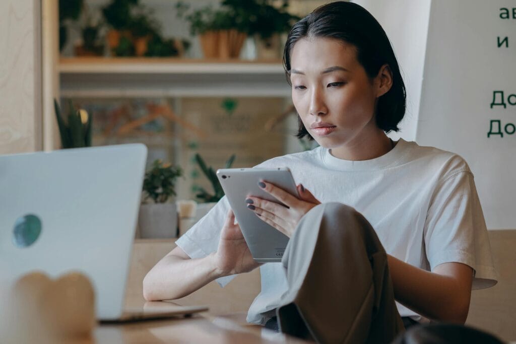 A woman sitting in a coffee shop, focused on her tablet computer.
