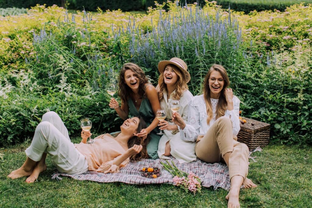 A group of four women relaxing on a picnic blanket in a vibrant garden.