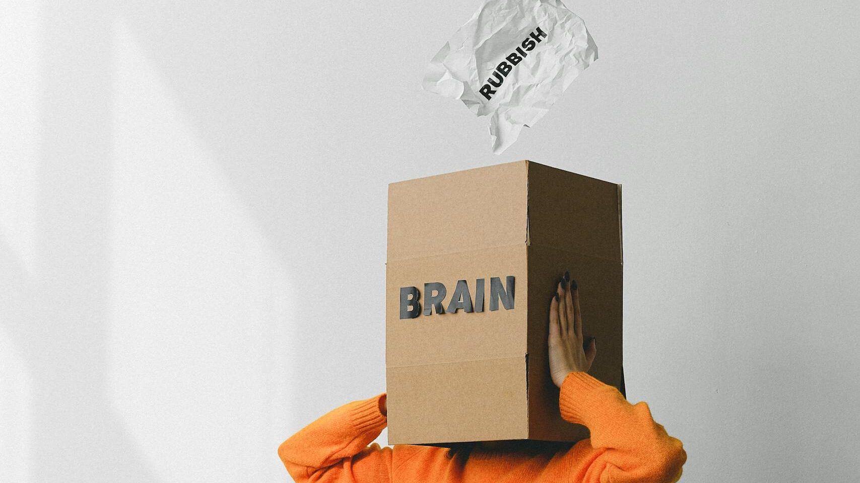 Crop anonymous person putting creased paper with Rubbish inscription in container with Brain title on head of female on chair. - 11 Ways To Reprogram The Subconscious Mind For Success
