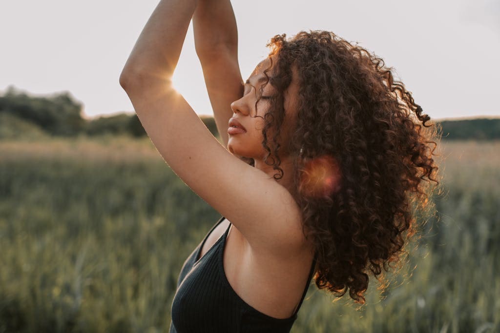 A fashionable woman with curly hair poses confidently outdoors during sunset. - How Can You Develop Emotional Intelligence In 8 Simple Steps