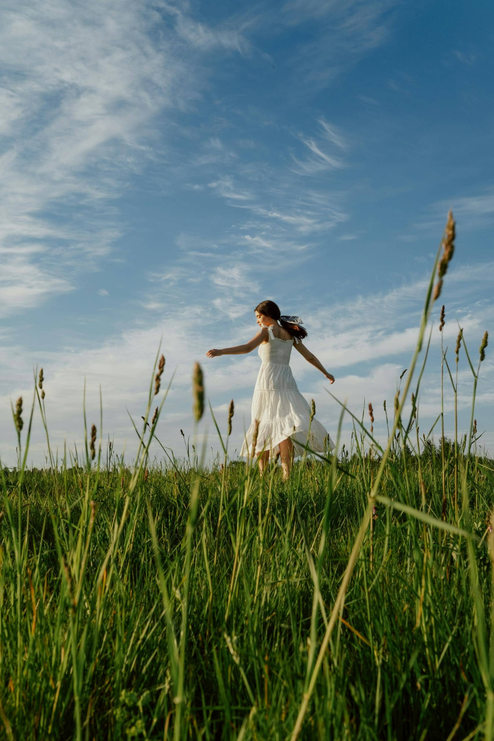 A woman in a white dress joyfully dances in a sunlit meadow against a clear blue sky. - How Can You Develop Emotional Intelligence In 8 Simple Steps