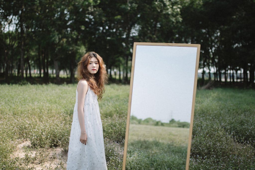 A young woman stands in a serene park, reflecting in a mirror under summer trees. - How Can You Develop Emotional Intelligence In 8 Simple Steps