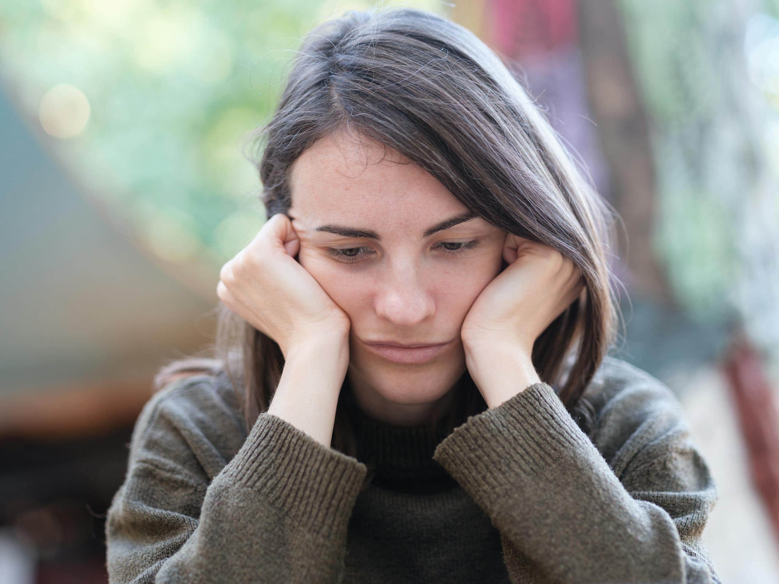 Portrait of a young woman looking pensive and thoughtful while sitting outdoors. - How To Avoid Negative People: Surround Yourself With Positivity